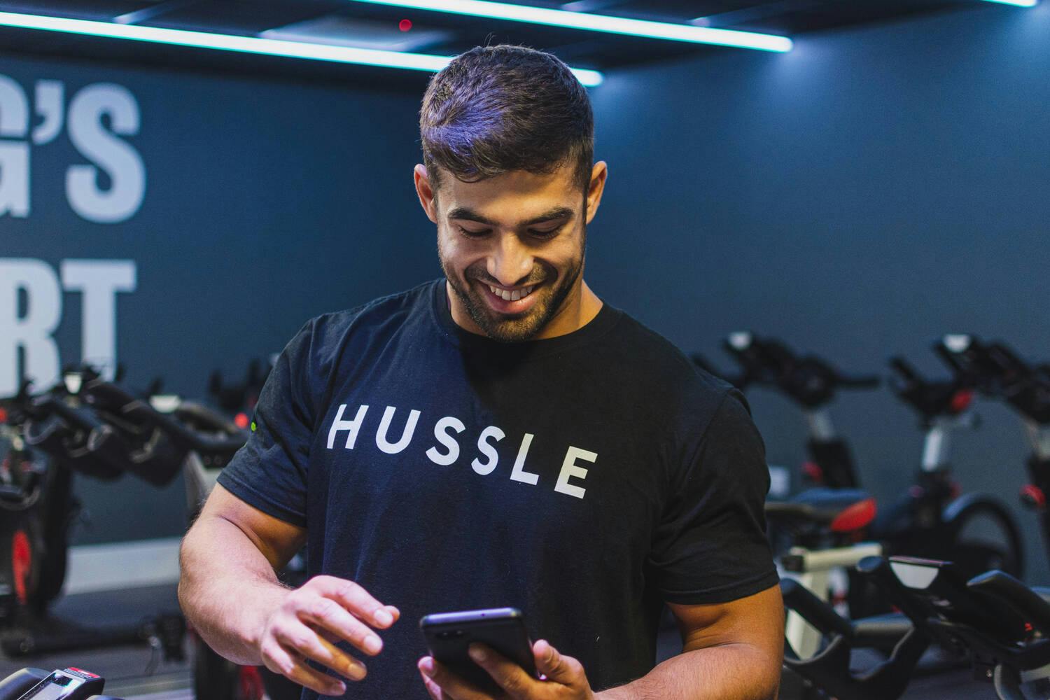 A man in a gym checking out the Hussle blog on their smartphone.