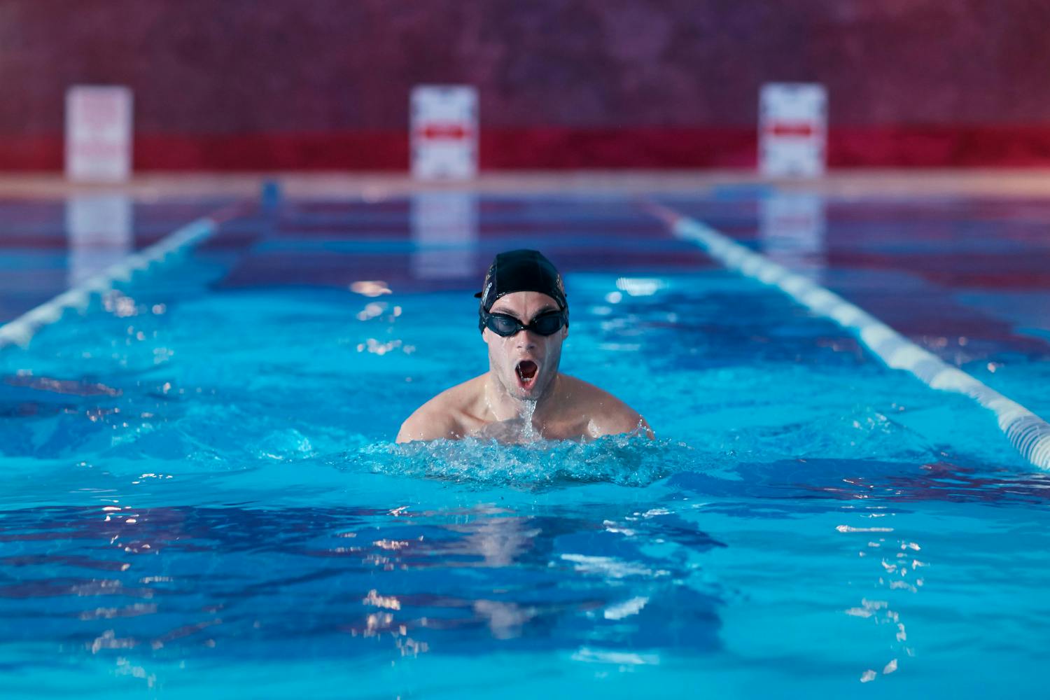 A man in a swimming cap and goggles swimming in a pool.
